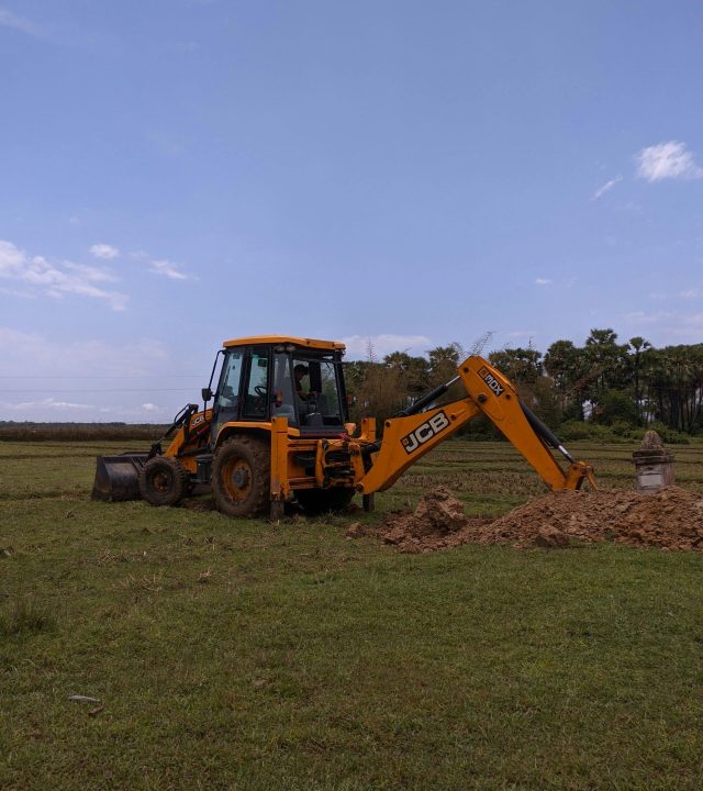 Excavator working with dirt in open grassy field under clear blue sky. Ideal for construction themes.