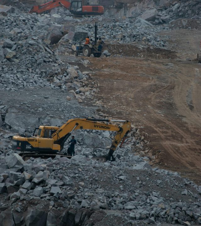 Heavy machinery working at a rocky quarry, showcasing industrial construction activity.