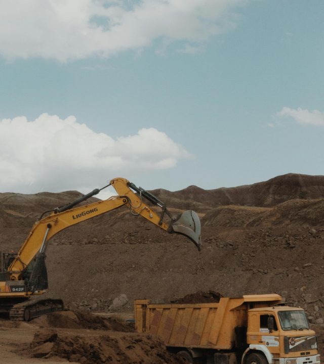 Yellow excavator and dump truck operating in a mining setting under a blue sky.