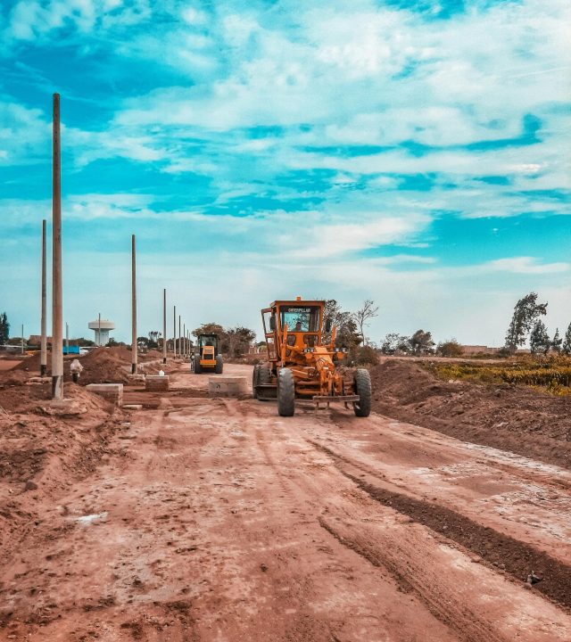 Yellow bulldozer working on a dirt road under a blue sky, ideal for construction themes.