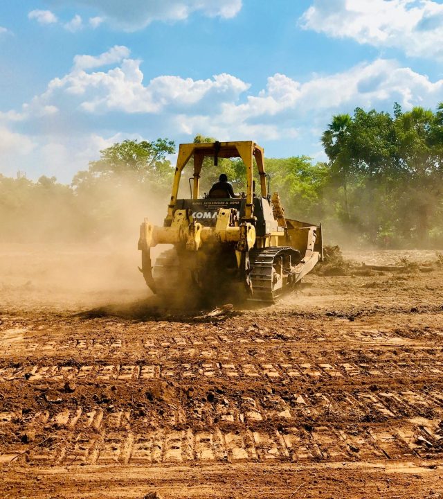 A yellow bulldozer working on a dusty construction site, moving earth under a clear sky.